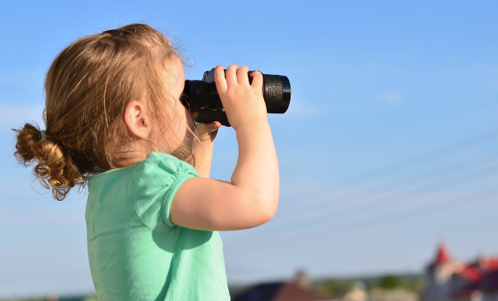 Child observing weather through binoculars on clear day.